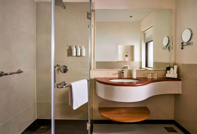 Modern bathroom with walk-in shower and curved wooden vanity at Mercure Goa Devaaya Resort Divar Island